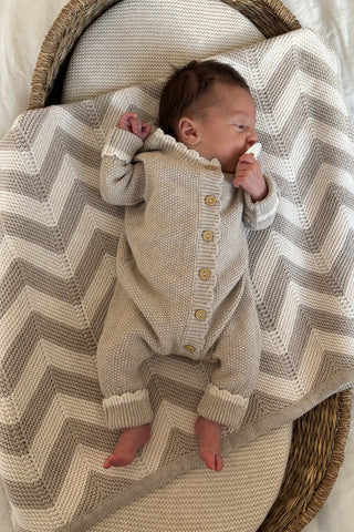newborn baby in basket lying on chevron knit blanket wearing knitted beige romper