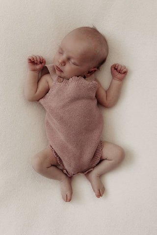 Sleeping newborn wearing a knitted pink baby romper
