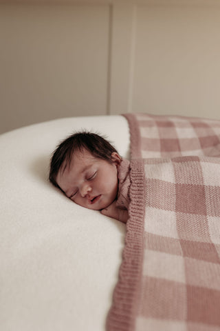 Sleeping newborn under a check pink and cream blanket