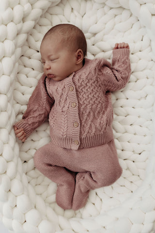 baby lying in knitted basket wearing knitted pink set