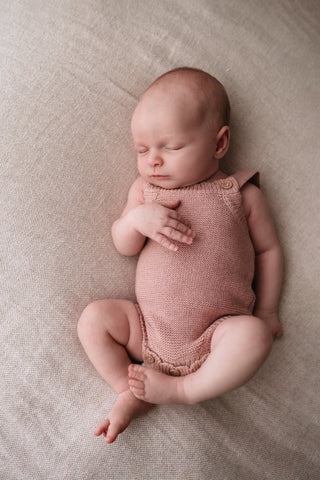 Sleeping baby wearing a pink knitted romper