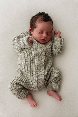 Baby wearing a light green knitted romper with buttons and scalloped edges