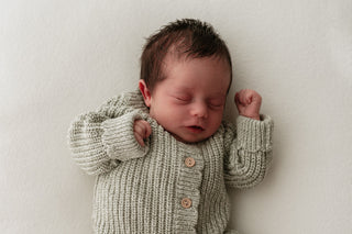 Baby wearing a light green knitted romper with buttons and scalloped edges