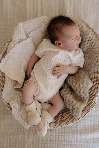 Sleeping baby in basket lying on blankets wearing knitted bodysuit and booties