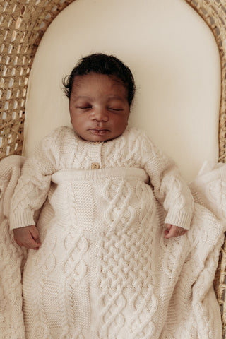 Sleeping baby in moses basket wearing cable knit cardigan and with a cable knit blanket