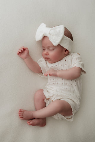 Baby wearing knitted white bow headband and pointelle knit bodysuit