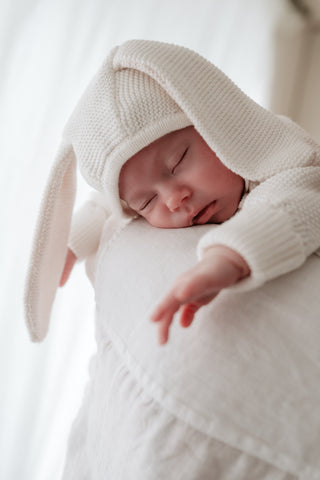 Baby sleeping on mother's shoulder wearing a knitted bunny ear bonnet
