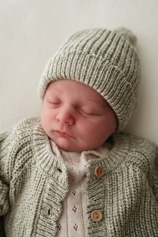 Sleeping baby wearing knitted green hat and cardigan