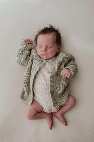 Baby wearing pointelle knit bodysuit and sage green chunky knit cardigan