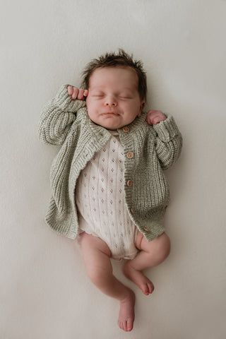 Baby wearing sage green knitted cardigan and neutral pointelle knit bodysuit