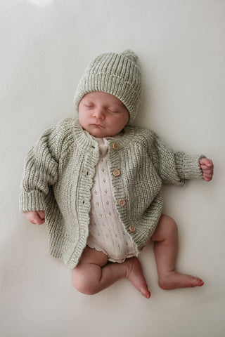 Baby wearing sage green knitted hat and matching cardigan