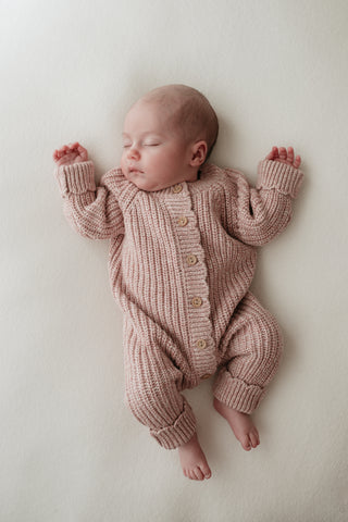 Sleeping baby wearing knitted pink romper 