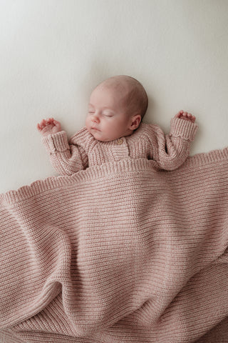 Sleeping baby wearing knitted pink romper and blanket with scalloped edge