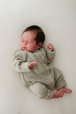 Sleeping baby wearing sage green knitted romper suit