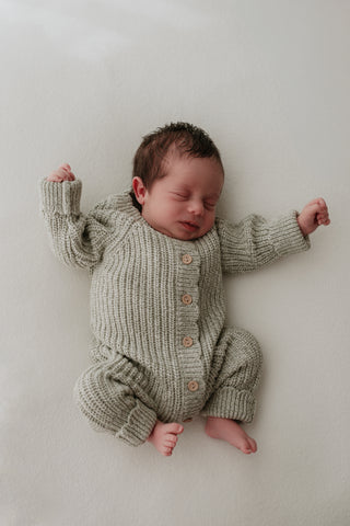 Stretching baby wearing sage green knitted romper suit
