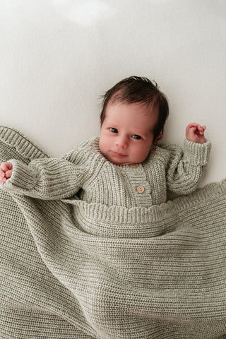 Baby wearing light green knitted romper and blanket