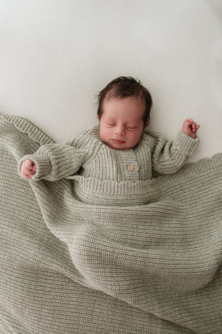 Baby wearing light green knitted romper and blanket
