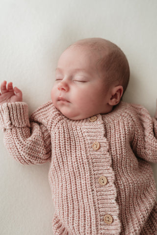 Sleeping baby wearing chunky pink knitted romper with buttons