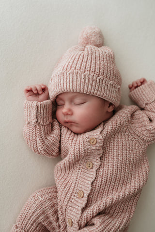 Sleeping baby wearing a light pink knitted outfit
