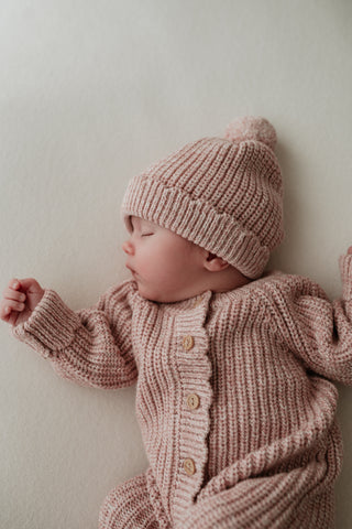 Sleeping baby wearing a light pink knitted outfit and hat