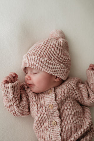 Sleeping baby wearing a light pink knitted outfit