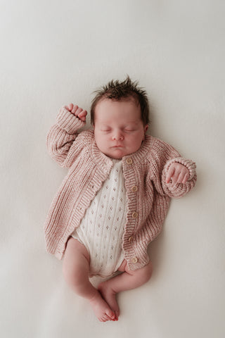 Baby wearing pointelle knit bodysuit and pink knitted cardigan 