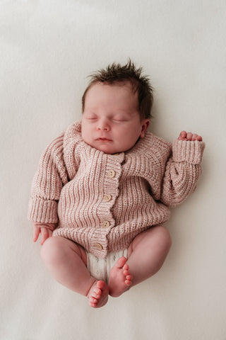 Sleeping baby wearing a light pink knitted cardigan