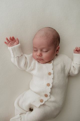 Baby sleeping wearing white button up knitted romper