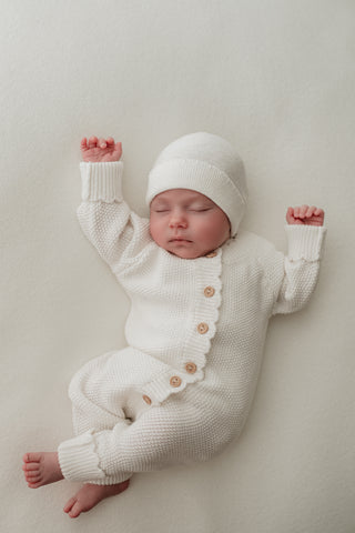 Sleeping baby wearing white knitted hat and romper
