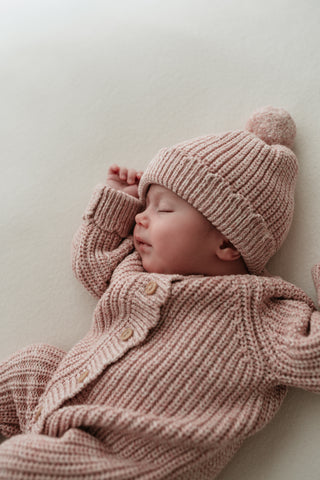 Sleeping baby wearing a light pink knitted outfit