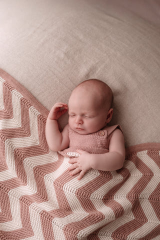 Newborn baby girl wearing a pink knitted romper with a pink chevron stripe knit blanket