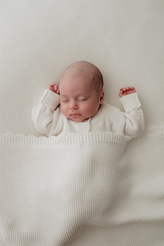 Baby sleeping under a white scallop blanket