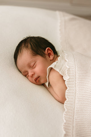 Sleeping baby wearing a beige knit romper with a scalloped edge beige knitted blanket