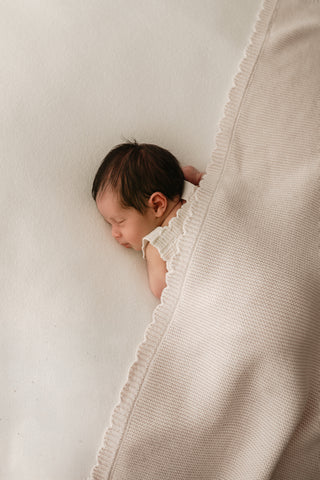 Sleeping baby with a scalloped edge beige knitted blanket