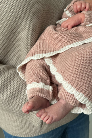 Baby wrapped in a pink knitted blanket with a cream scalloped trim 