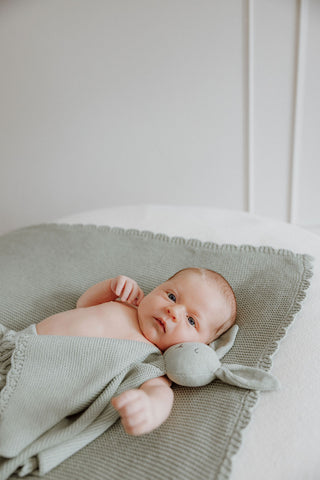 Newborn Baby cuddling Knitted Sage Bunny Comforter lying on a Knitted Sage Baby Blanket