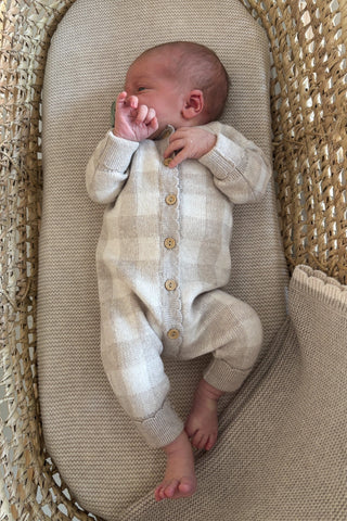 baby in moses basket with blanket and wearing checkered knit romper