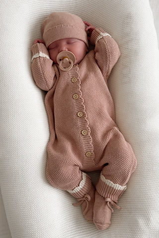 Sleeping baby with dummy wearing pink knitted hat, romper and booties