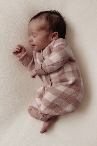Smiling newborn baby wearing pink checkered knit romper