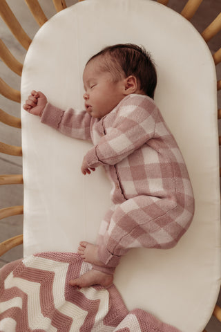 Sleeping baby in cot wearing pink check knit romper with pink stripe knit blanket