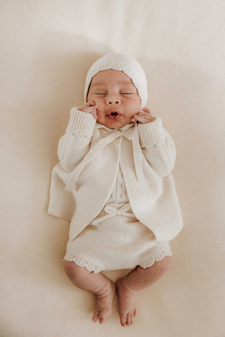 Baby wearing knitted bonnet, cardigan ans bloomers