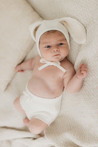 Baby wearing a bunny ear knitted bonnet with matching white bloomers