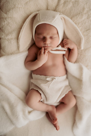 Sleeping newborn baby in a knitted bunny ear bonnet and bloomers
