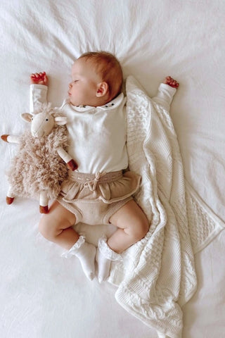 Sleeping infant with cuddly lamb and white knitted baby blanket
