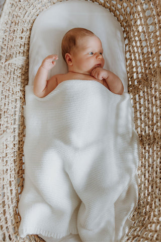 Baby in moses basket with white knitted baby blanket