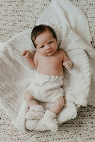 Baby in basket with knitted baby blanket, bloomers, and booties