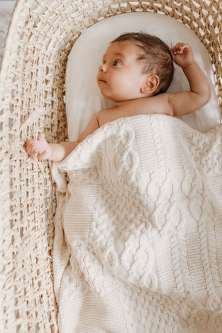 Baby in moses basket with cable knit blanket