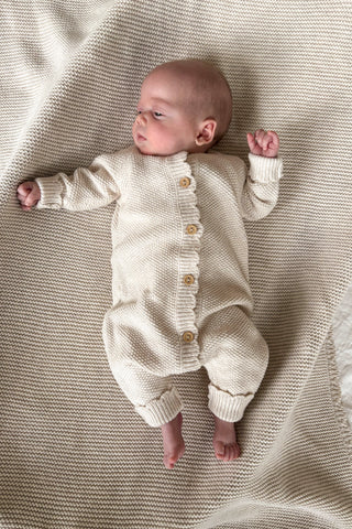 newborn baby in basket lying on beige knitted blanket wearing beige knitted romper 