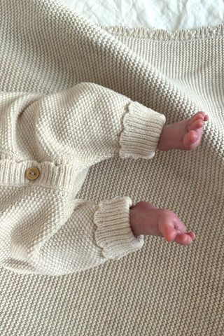 Baby's feet, wearing knitted romper and lying on beige knitted blanket