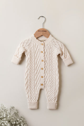 Organic cotton cable knit romper in oat colour on a wooden Isla & Fraser hanger.
